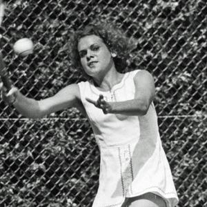 Evonne Goolagong-Cawley holding a wooden tennis racket and about to hit a tennis ball.