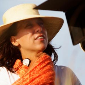 Director Rachel Perkins, wearing a broad-brimmed hat and bright orange scarf, looking through a camera lens