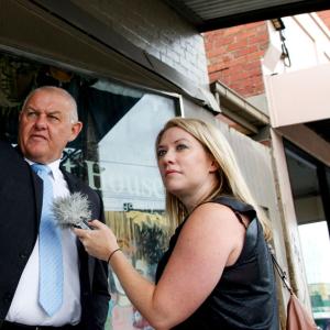 Rachael Brown interviewing policeman Ron Iddles in front of a store on a street.