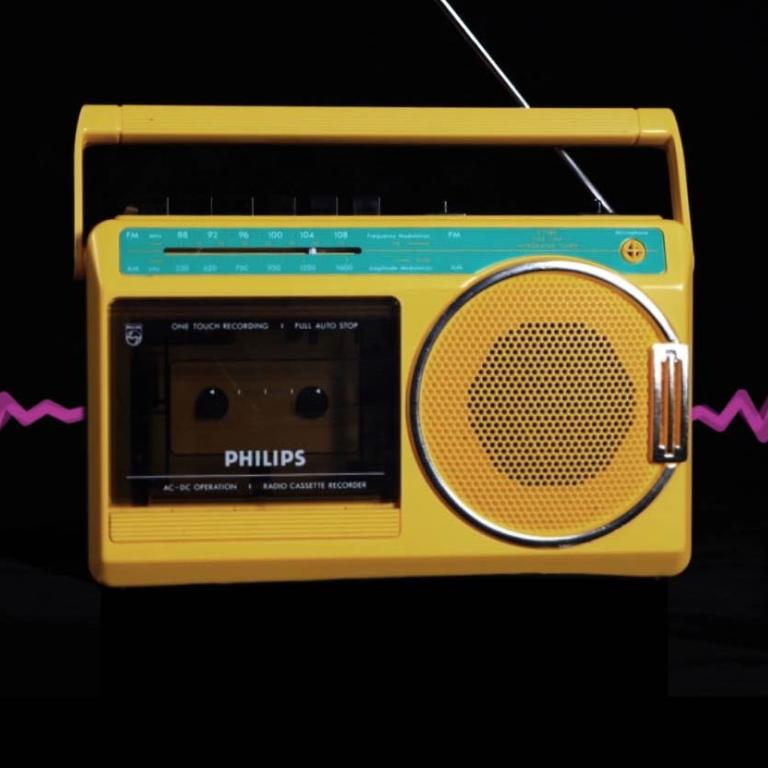 A yellow 1980s radio cassette player pictured in front of a pink radio wave